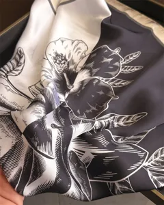 Close-up detail of black and white botanical print silk square scarf, elegant fabric texture.