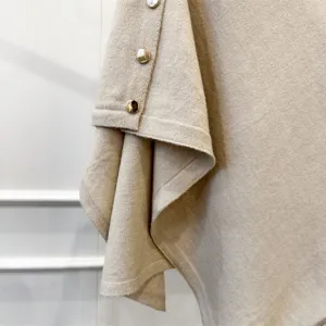 Knitted cape detail shot, beige wool shawl texture closeup, elegant metal button decoration.