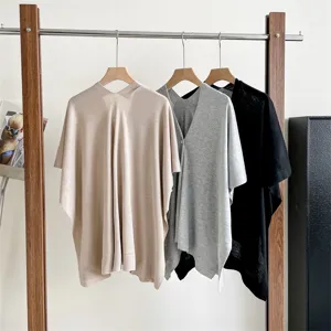 Detailed view of lightweight summer knit shawl and poncho hanging on wooden rack, casual style.