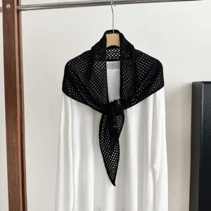 Close-up view of black crochet knit triangular shawl layered over white long sleeve shirt.