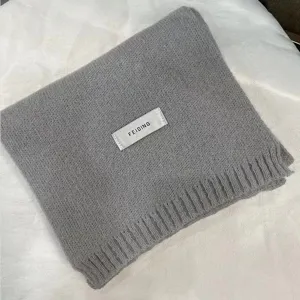 Grey knitted scarf detail showing soft texture and brand label design for winter cold weather.