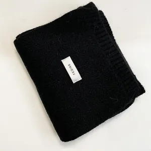 Detailed close-up shot of a cozy black knitted winter scarf, neatly folded with a fabric label.