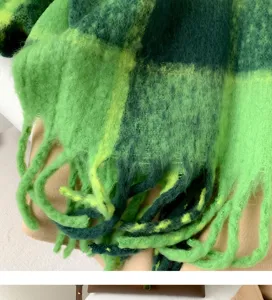 Close-up detail shot of soft green plaid fuzzy winter scarf showing rich fringe texture.