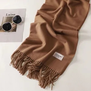 Primo piano dettagliato di una sciarpa tinta unita spessa con frange e etichetta su sfondo bianco.