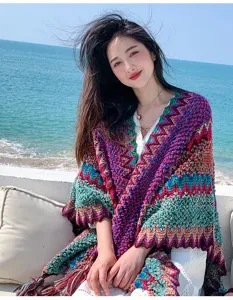 Detailed view of colorful ethnic knit poncho, cozy woolen cape worn by model on sunny beach.
