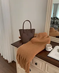 Detailed scene of a brown leather bucket bag and thick camel mohair tassel scarf on dresser.