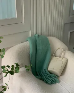 Close-up detail of cozy green mohair thick knitted scarf with fringe draped on white chair.