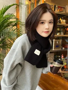 Detail shot of a cozy black knitted winter scarf worn by a model in a cafe setting.
