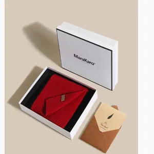 Close-up detail of a red wool knitted scarf inside an elegant white gift box with brand logo.