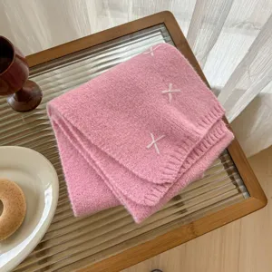 Pink knitted wool blend scarf detail, cozy winter neck wrap with white cross embroidery.