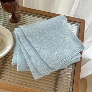 Soft light blue knitted woolen scarf detail featuring cute white embroidered bow accents.
