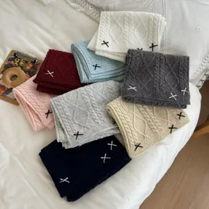 Detailed view of cozy knit winter scarves with cute bow embroidery displayed on a soft bed.