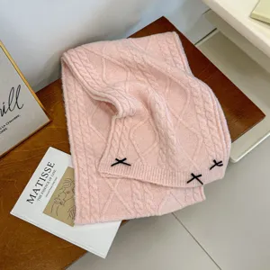 Pink knitted winter scarf with cute black bow decoration, cozy cable knit fabric accessory.