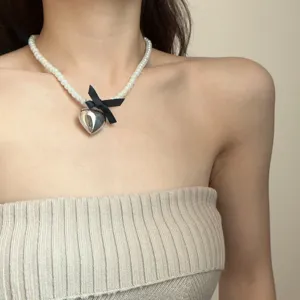 Close-up detail of the pearl necklace featuring a silver heart pendant and a black bow.
