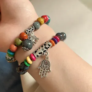 Vista detallada de pulseras étnicas de cuentas de cerámica y madera con dijes plateados.