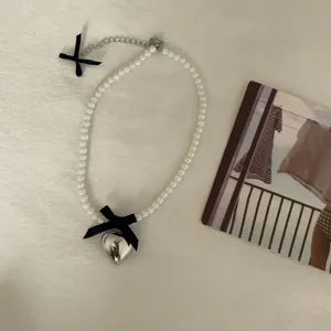 Close-up detail of the sweet pearl necklace with silver heart pendant and cute black bows.