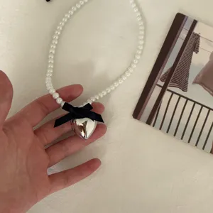 Close-up detail of a sweet pearl necklace with a silver heart pendant and black bow.