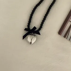 Detailed close-up of the black beaded necklace featuring a fabric bow and silver heart.
