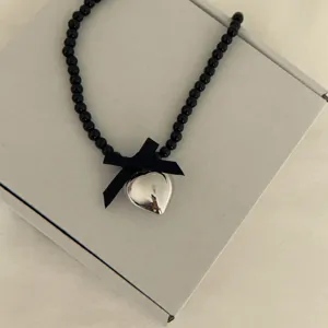 Chic black beaded necklace with cute ribbon bow and silver heart pendant for sweet summer style.