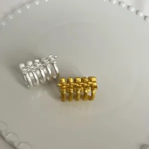 Gros plan de larges bagues géométriques argentées et dorées sur fond blanc et propre.