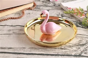 Close-up detail of the cute pink ceramic flamingo figurine standing inside a shiny gold jewelry tray.