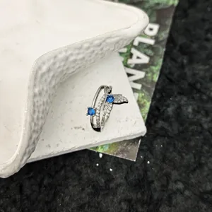 Detail d'une bague ouverte en argent avec un design de queue de baleine et des zirconies bleues.