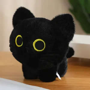 Close-up detail shot of cute black cat plush toy with big yellow embroidered eyes on desk.