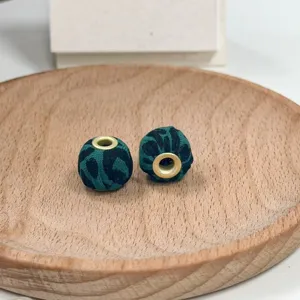 Close-up detail of green leopard print fabric beads with metal eyelets on wood plate.