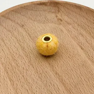 Close-up detail of yellow felt ball bead with metal eyelet for handmade jewelry making.