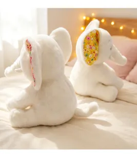 Cute glowing elephant plush toy detail showing soft white fabric and floral ears on bed.