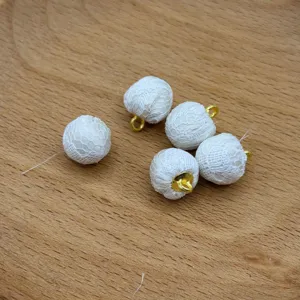 White lace fabric covered beads with golden metal loops, detail view of DIY jewelry accessories.