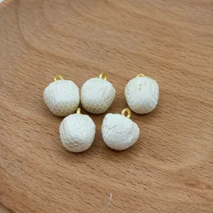 Detail view of white lace fabric wrapped ball charms with gold loop for DIY jewelry craft.