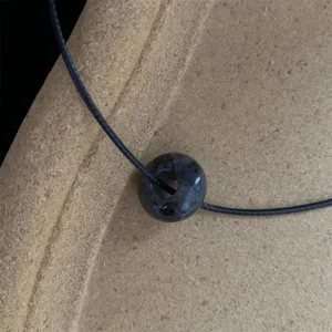 Detailopname van de elegante donkere edelsteen donuthanger en zwarte koord ketting.