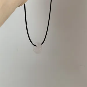 Gedetailleerd overzicht van een minimalistische roze stenen ringketting op zwart koord.