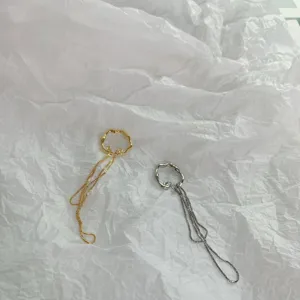 Detailansicht unregelmäßiger Metall-Ohrklemmen mit doppelten Ketten in Gold und Silber.
