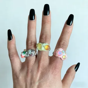 Gros plan détaillé de bagues empilables en résine colorée faits main sur les doigts, design unique.