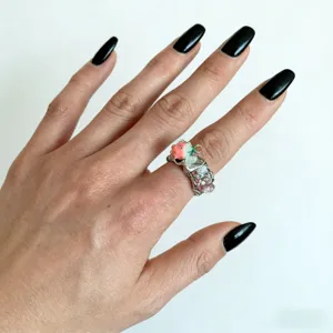 Gros plan d'une bague ouverte artisanale sur le thème de la fraise avec des pierres colorées.