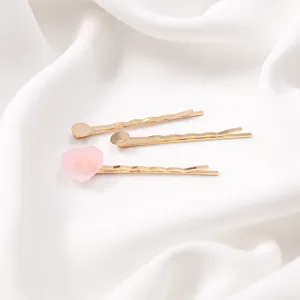 Detailed shot of three gold bobby pins with one cute pink heart accessory on white fabric.