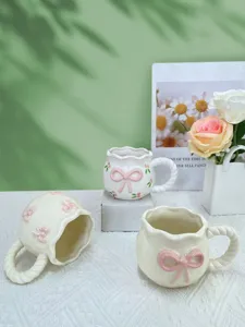 Gros plan sur la tasse en céramique mignonne avec nœud rose et anse torsadée, décor cosy.