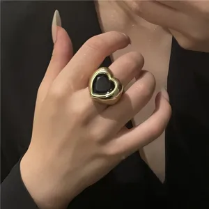 Gros plan détail de bague dorée épaisse avec pierre précieuse cœur noir, bijou.
