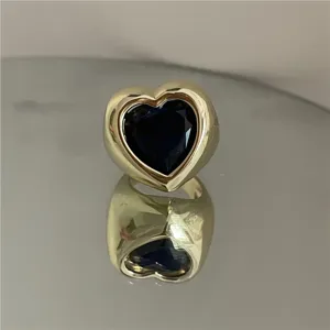 Gros plan détaillé d'une bague cœur massive dorée avec une pierre précieuse bleu foncé.