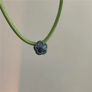 Detail shot of a niche designer green PU leather choker necklace with a purple crystal flower.