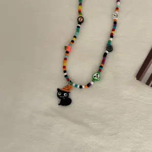 Detailopname van een handgemaakte Halloween kraal ketting met zwarte kat hanger en kleurrijke kralen.