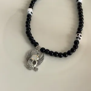 Gotische punk stijl zwarte kralen ketting met zilveren gevleugelde schedel hanger detail.