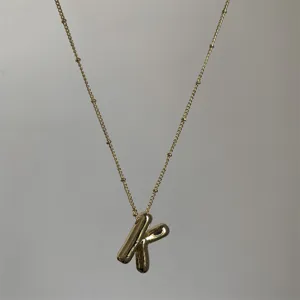 Detailopname van de vergulde puffy letter K hanger halsketting met fijne kralenketting.