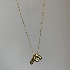 Detailopname van een vergulde ketting met dikke letter F hanger en fijn kraalkettinkje.