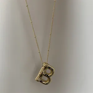 Gouden dikke letter B hanger detailopname, fijne kraaltjes ketting close-up weergave.
