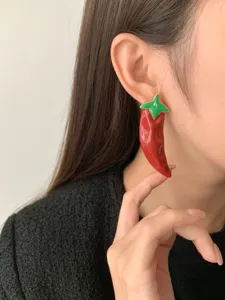 Close-up detail of bold red chili pepper earrings with green enamel leaves, statement style.