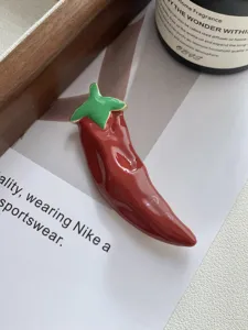 Close-up detail shot of red enamel chili pepper brooch with gold trim, stylish display.