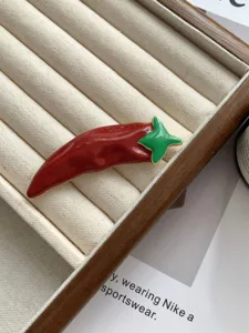 Enamel red chili pepper brooch detail with vibrant red and green color contrast.